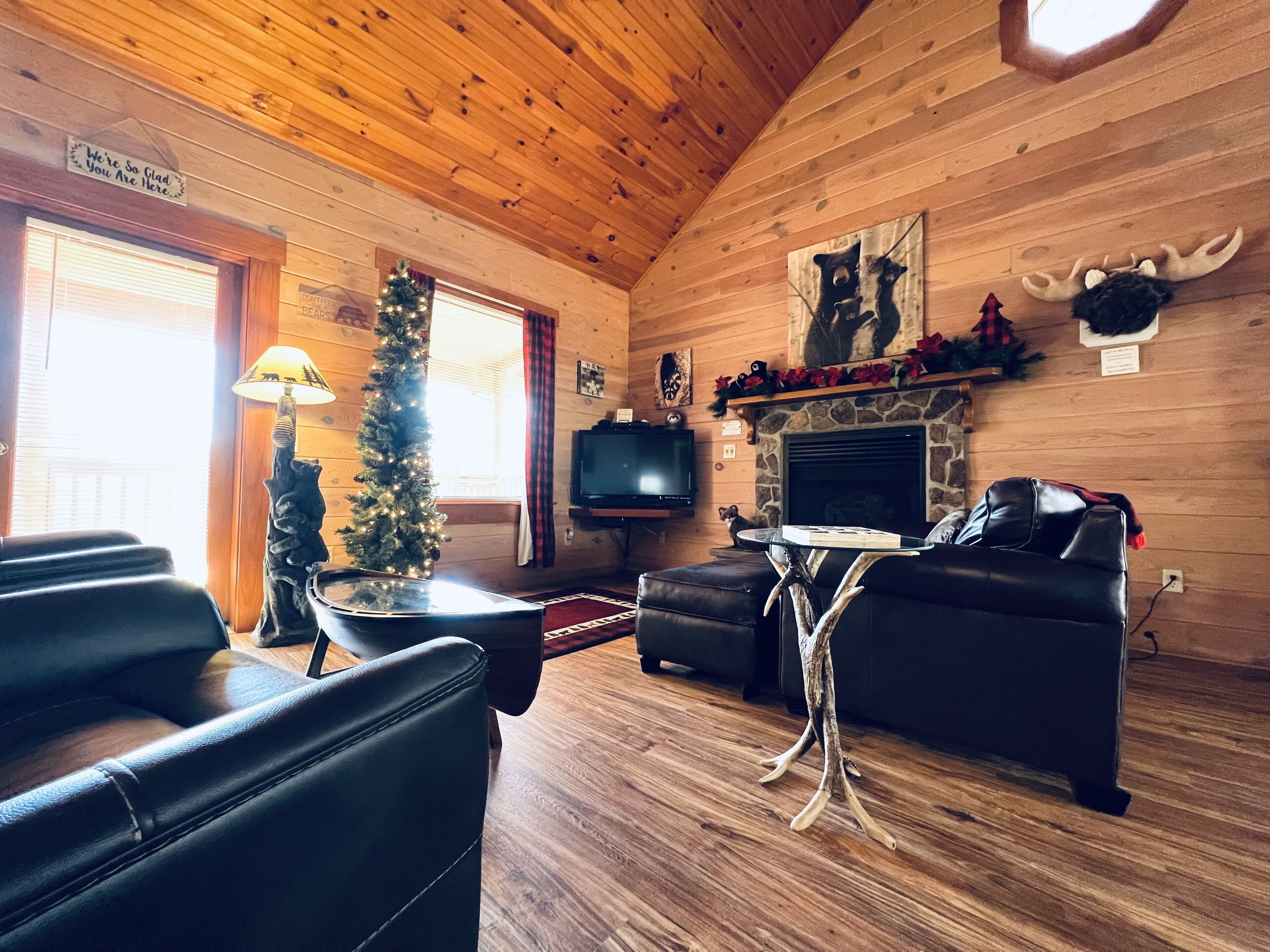 A cozy cabin interior with wooden walls, a fireplace, a television, and a Christmas tree.