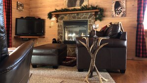 Un acogedor interior de cabaña con chimenea, mobiliario de cuero y un televisor.