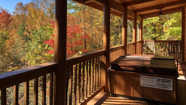 A wooden deck with a hot tub, surrounded by autumn foliage.