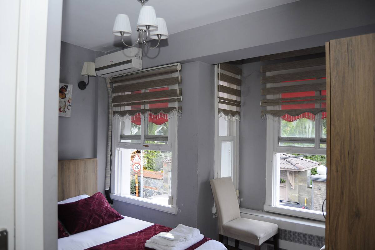 Quarto com cama, cadeira, janela com vista para o exterior e luminária no teto.