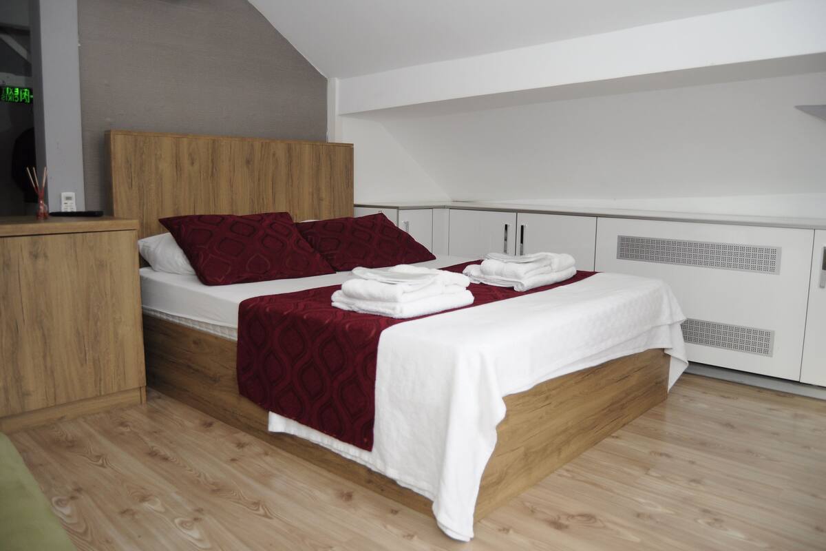 Quarto moderno com estrutura de cama de madeira, roupa de cama branca e manta vermelha.