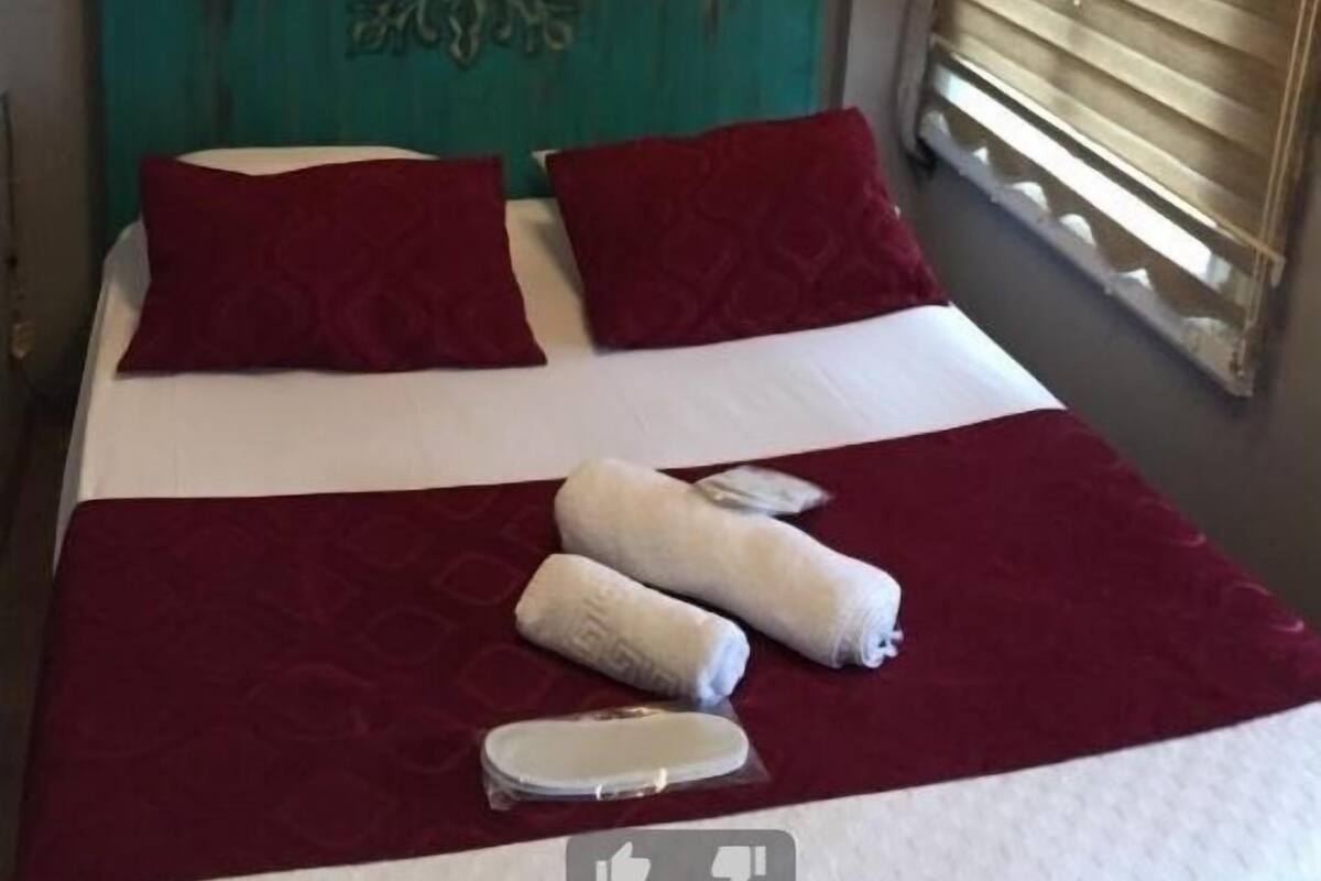 Uma cama com roupa de cama vermelha e branca, duas almofadas vermelhas e duas toalhas enroladas.