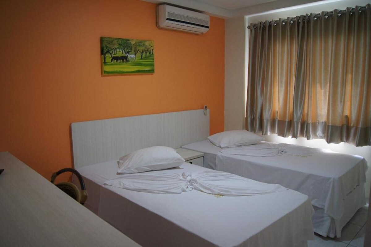 Une chambre d’hôtel avec deux lits, un climatiseur, un tableau au mur et une fenêtre avec des rideaux.