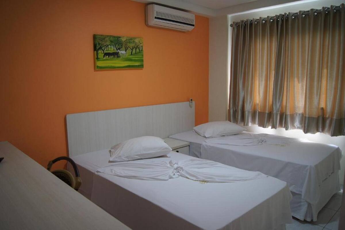 Une chambre d’hôtel avec deux lits, un climatiseur, un tableau au mur et une fenêtre avec des rideaux.