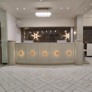 A reception desk with a modern design, featuring a large window with decorative lighting and a ceiling light fixture.