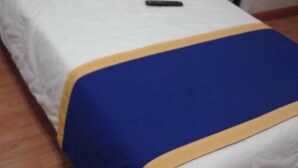 A single bed with a white mattress, a blue and yellow bedspread, and a black bag on the floor beside it. - Hotel Sierra Gorda (Ciudad Victoria)