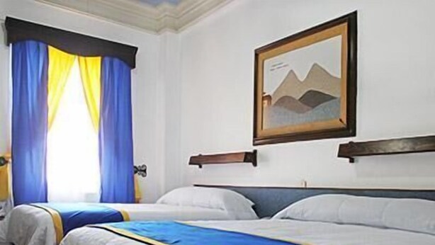 A hotel room with two beds, a painting on the wall, and a window with blue curtains. - Hotel Sierra Gorda (Ciudad Victoria)