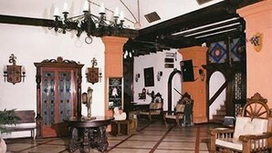 A spacious living area with a tiled floor, a wooden chair, a table, and a decorative cabinet. - Hotel Sierra Gorda (Ciudad Victoria)