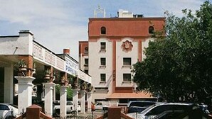 A building with a white facade, multiple windows, and a red roof. There are cars parked in front and a tree to the right. - Hotel Sierra Gorda (Ciudad Victoria)