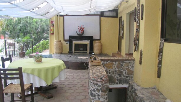 A patio area with a stone wall, a fireplace, and a table with chairs. - Hotel Teocalli (Tepoztlán)