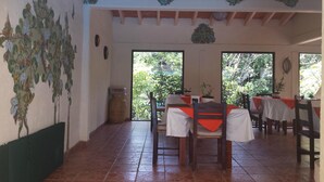 A dining area with a rustic interior, featuring a tiled floor, wooden chairs, and tables covered with white tablecloths. - Hotel Teocalli (Tepoztlán)