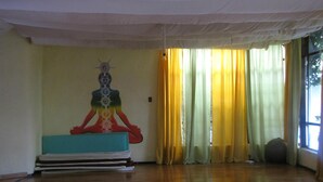 A room with a wooden floor, a meditation mat, a wall with a geometric design, and a window with yellow curtains. - Hotel Teocalli (Tepoztlán)