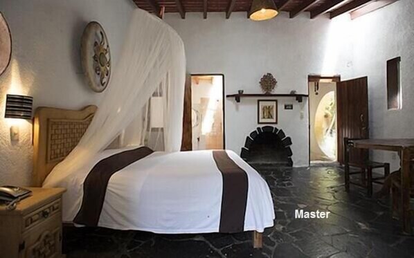 A master bedroom with a bed, a fireplace, a stone floor, and a wooden ceiling. - Hotel Teocalli (Tepoztlán)