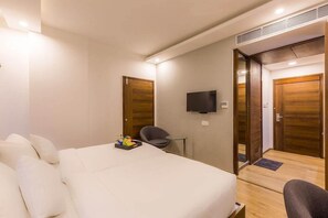 Habitación de hotel con cama, televisión, sillón y puertas de madera.