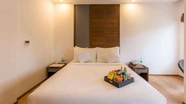 Habitación de hotel con una cama grande, mesitas de noche, una mesita auxiliar, un cabecero de madera y una bandeja de aperitivos sobre la cama.