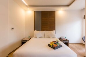 Een hotelkamer met een groot bed, nachtkastjes, een houten hoofdeinde en een schaal met snacks op het bed.