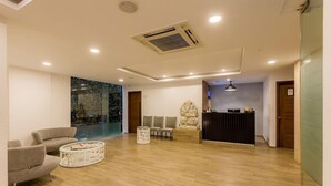 Un área de recepción moderna con mostrador, zona de estar y un ventanal con vistas a una piscina.