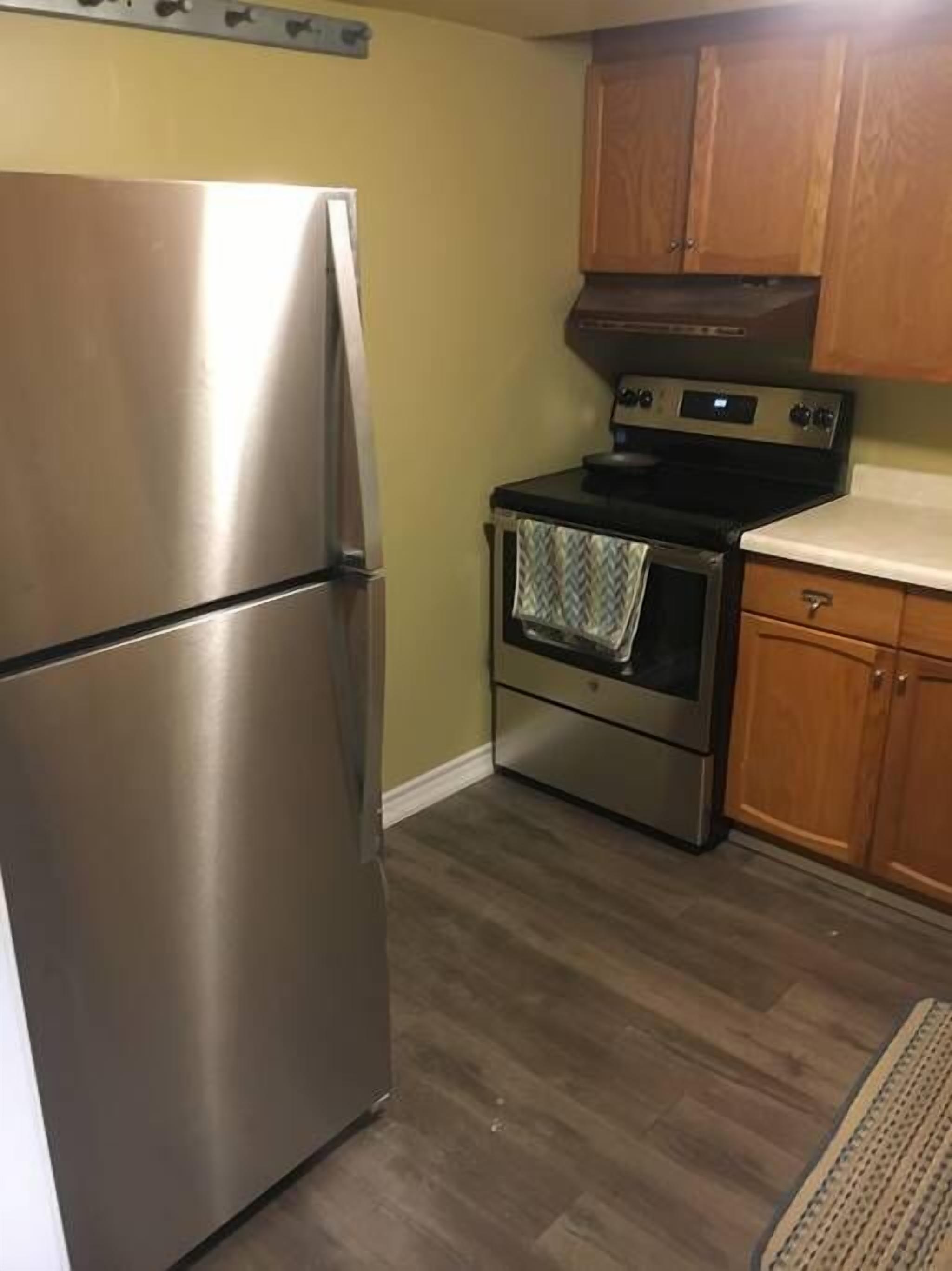A compact kitchen with a stainless steel refrigerator, a built-in oven, and wooden cabinets.