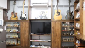 Een kamer met een houten kast waarin gitaren, een televisie en diverse spullen op planken staan.