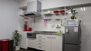 Een moderne keuken met witte kasten, een roestvrijstalen koelkast, een magnetron en een spoelbak. Aan de muur hangt een brandblusser en op het aanrecht staat een plant.