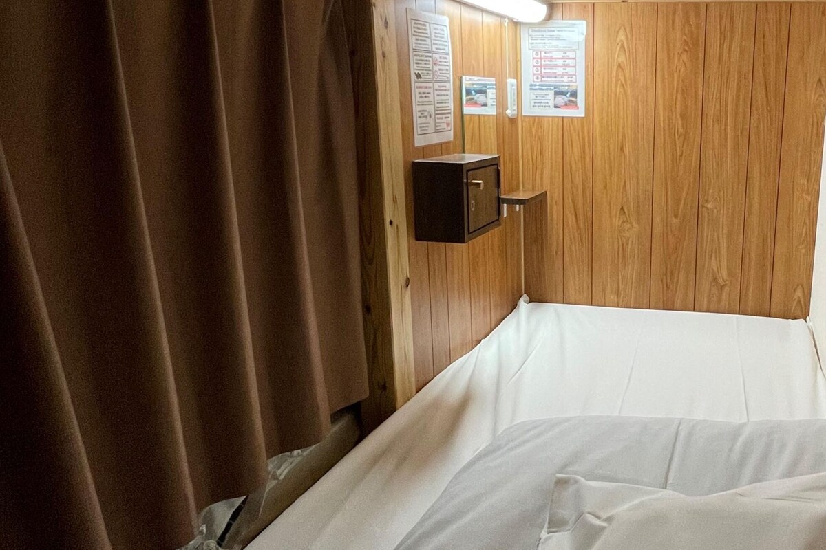A single bed with white linens in a cabin-style room with wooden walls and a ceiling.
