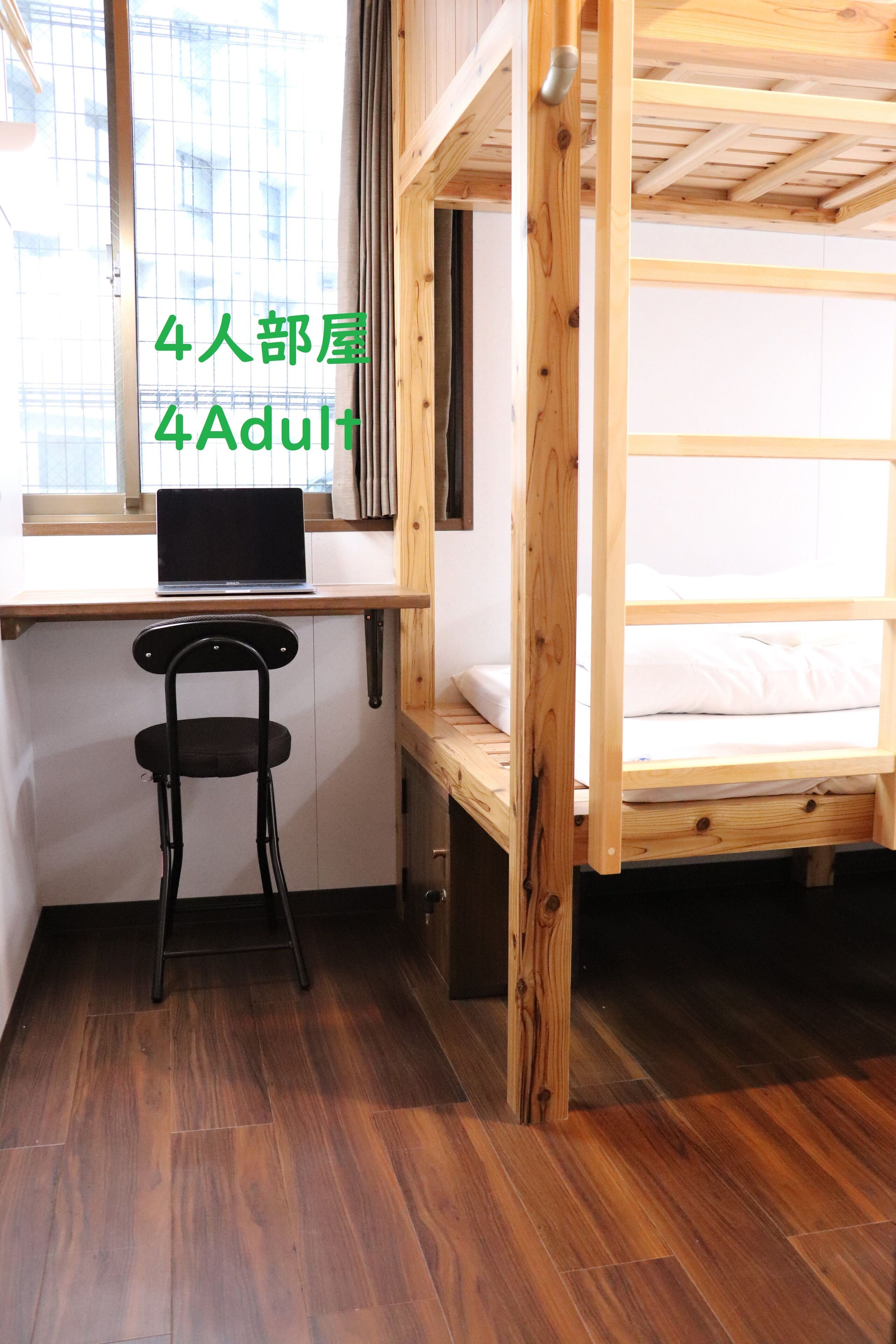 A 4-person dormitory room with a wooden bunk bed, a desk with a laptop, and a chair.