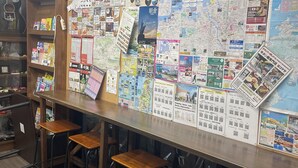 Een bar met een houten toonbank, meerdere stoelen en een muur bedekt met diverse informatieposters en kaarten.