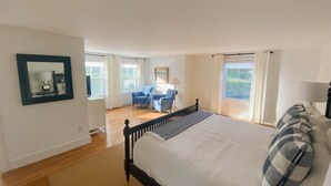 Ein Schlafzimmer mit einem großen Bett, zwei Stühlen, einem Spiegel und einem Fenster mit Vorhängen.