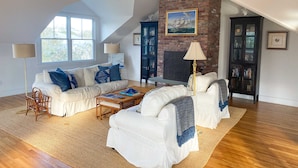 Ein geräumiger Loft mit hoher Decke, freiliegender Backsteinwand und großen Fenstern. Es gibt eine weiße Sofagarnitur, einen Couchtisch und eine Lampe.