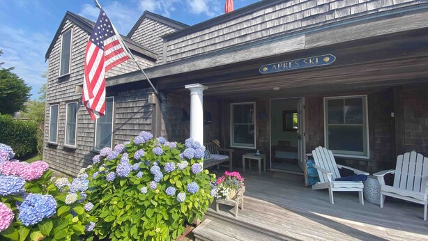 Ein Holzhaus mit Veranda, einer amerikanischen Flagge und einem Schild mit der Aufschrift 'APRES SKI'.