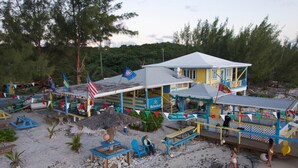 Un bâtiment situé en bord de mer, avec une enseigne Heineken, des places assises en plein air et une structure dotée d’un toit de chaume.