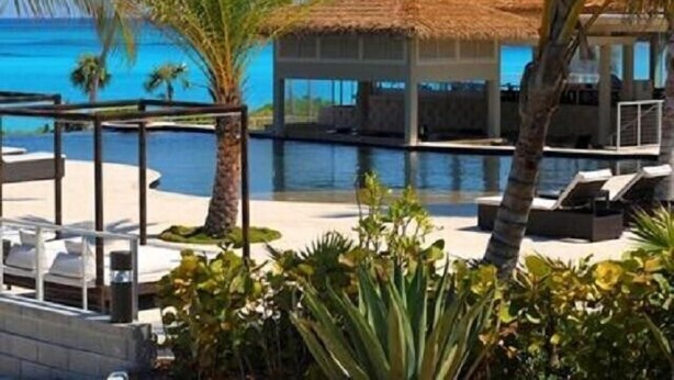 Un espace aménagé au bord de la piscine, avec des chaises longues, une structure à toit de chaume et une vue sur l’océan.