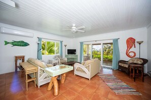 A spacious living room with a ceiling fan, a television, and a large window with a view of palm trees.