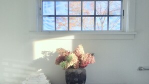 A room with a wooden dresser, a vase with flowers, and a window with a view of trees. - Fabulous Cottage on Pristine Broad Bay (Waldoboro)