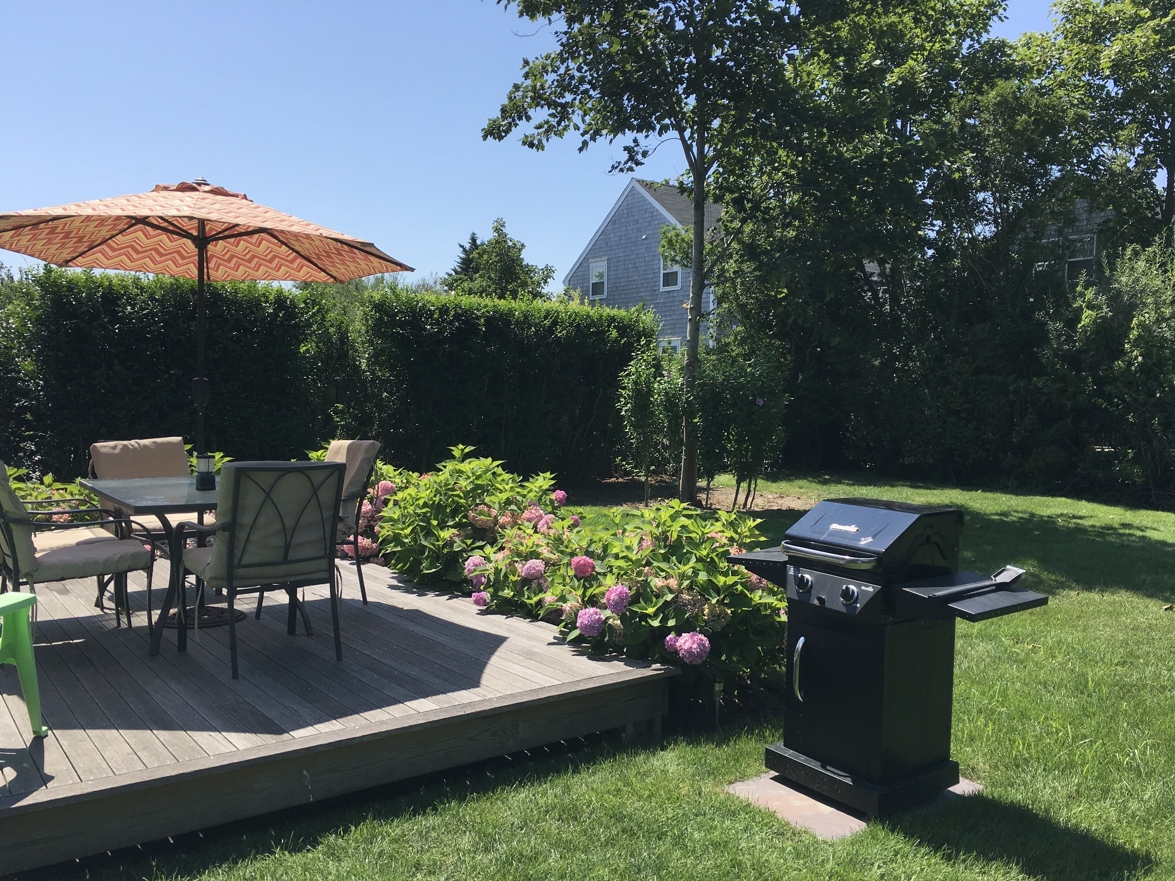 Een terras met tafel, stoelen, een barbecue en een grote parasol.