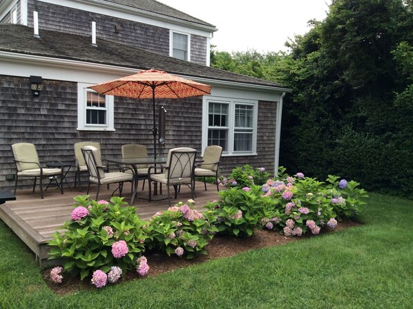 A deck with outdoor furniture and a large umbrella, surrounded by a garden with hydrangea plants.