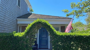 Una casa con puerta azul, una bandera estadounidense y un seto bien cuidado.