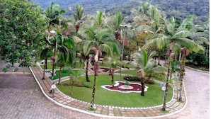 A landscaped area with palm trees and a circular garden, surrounded by a brick pathway and a road with a speed limit sign. - Cozy House in Gated Community -3 bedrooms (1 suite)-3 bathrooms-Internet (Massaguaçu)