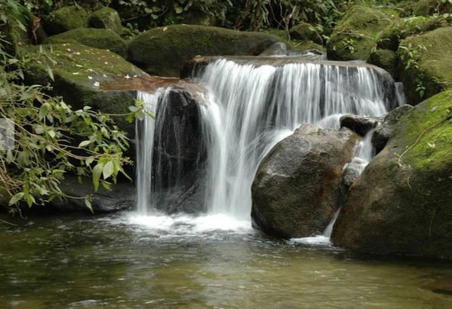 A waterfall cascading over moss-covered rocks in a forested area.