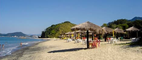A beach with thatched umbrellas and beach chairs, a clear sky, and a calm sea.
