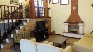 A living room with a fireplace, a TV on a stand, a staircase, and a sofa. - Cozy House in Gated Community -3 bedrooms (1 suite)-3 bathrooms-Internet (Massaguaçu)