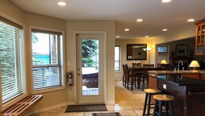 A kitchen with a bar area, wooden flooring, and a view through a glass door. - Deluxe Suite w/BBQ, Hot Tub, Laundry - Just minutes walking to village (Silver Star Mountain)