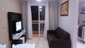 A living room with a TV, a sofa, a dining table, and a kitchen area. - Beachfront location - Ocean view - Market + Wi-Fi, Cable TV, and Netflix! (Praia Grande)