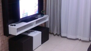 A living room with a flat-screen TV on a white entertainment unit against a brick wall. - Beachfront location - Ocean view - Market + Wi-Fi, Cable TV, and Netflix! (Praia Grande)