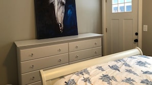 Une chambre à coucher avec un lit, une commode, une porte et un tableau représentant un cheval accroché au mur.