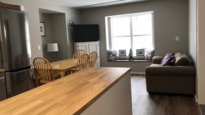 Une cuisine moderne avec un îlot central en bois, un coin repas avec des chaises, un téléviseur encastré et une fenêtre offrant une belle vue.
