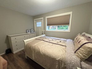 Un dormitorio con cama, cómoda, ventana con persianas y una puerta.