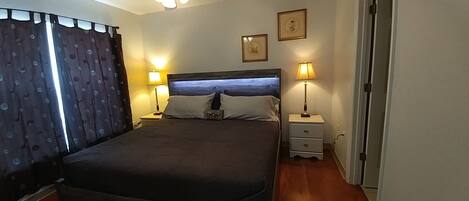 A bedroom with a large bed, two bedside tables with lamps, a ceiling fan, and two framed pictures on the wall.