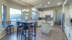 A spacious kitchen with a central island, bar stools, and a large window providing a view of the outdoors. - Golf Course & Mt VIEWS: Htd POOL, Hot Tub, Putting Green, Fire Pit, 3 Bikes (Mesa)