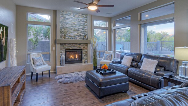 A spacious living room with a fireplace, leather furniture, large windows, and a ceiling fan. - Golf Course & Mt VIEWS: Htd POOL, Hot Tub, Putting Green, Fire Pit, 3 Bikes (Mesa)